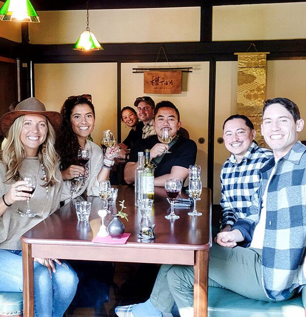 A group of smiling people enjoying a Koshu wine tasting and savoring local foods during a Winery Tours Japan experience at a winery in Yamanashi, Japan.